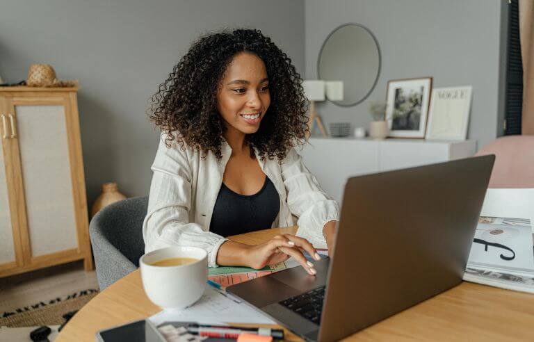 Black woman smiling while working looking for stock photo images on her laptop