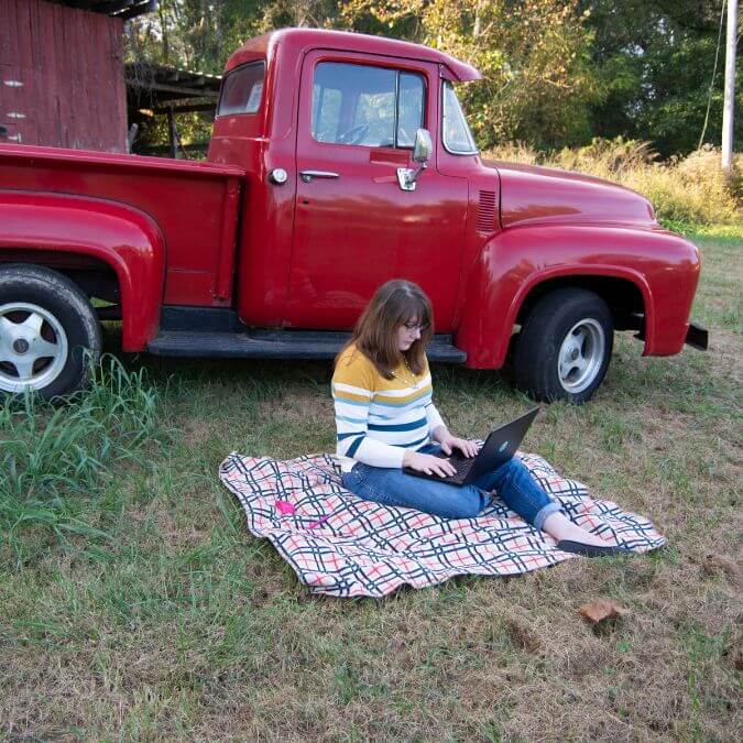 Paula Hickey sitting on a blanket outside working on her laptop