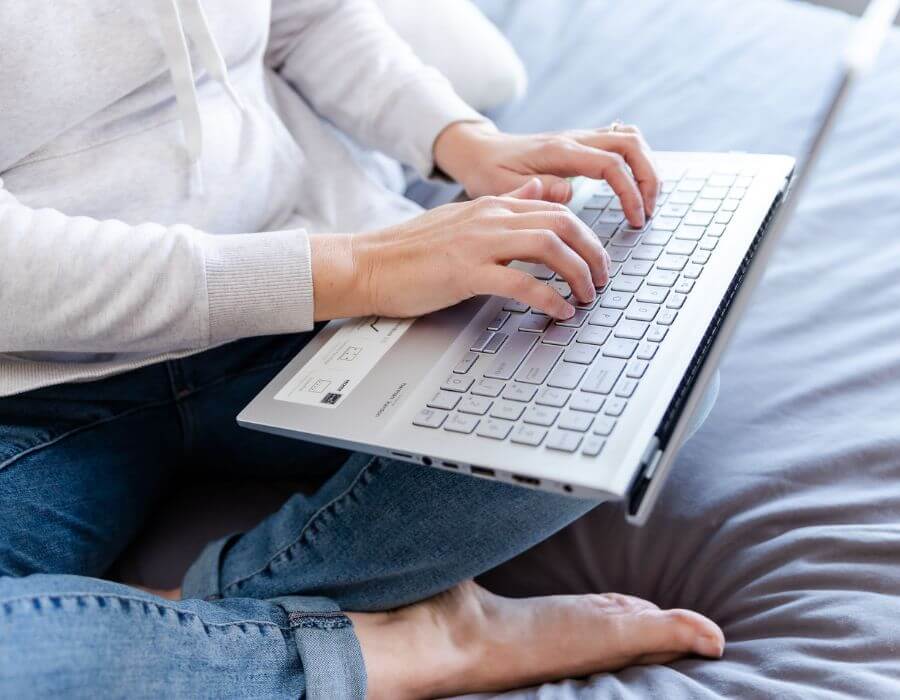 Woman sitting on bed cross legged with laptop on lap typing