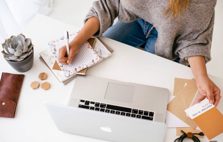 Woman in front of open laptop writing on a notepad and looking at color swatches