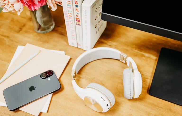 headphones, iphone, books, papers, pen on a wooden desk
