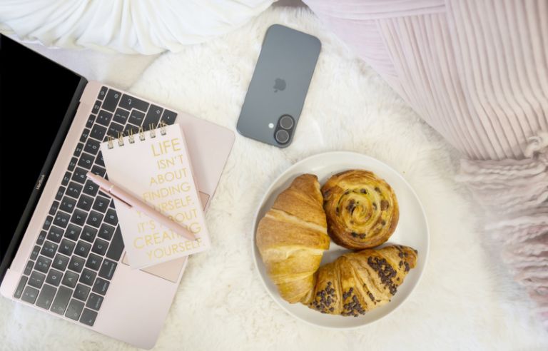 open laptop, iphone, pastries on a plush couch flatlay view